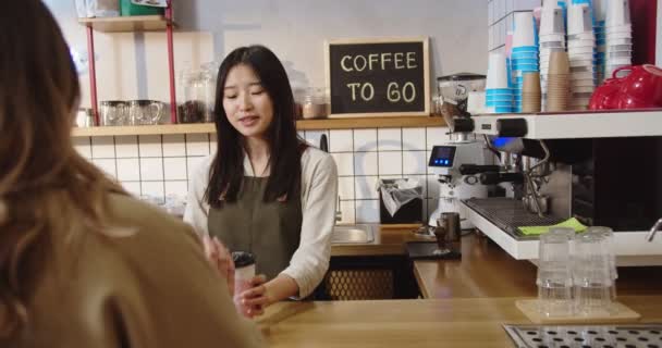 Güzel bayan müşterinin kahvehaneden siparişi alışının arka görüntüsü. Genç bayan barista içecek veriyor, müşteriyle konuşuyor ve menü haberlerini sunuyor. İş, hizmet, girişimcilik. — Stok video