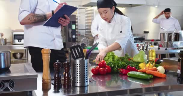 식당 주방에서 일하는 혼혈 청소년들의 모습. 아시아 여성 요리사는 백인 남성 관리자와 대화하기 위해 야채 제품을 선택 한다. 요리, 요리 컨셉트 — 비디오