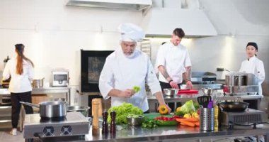 Yakışıklı, Kafkasyalı, kıdemli, yaşlı aşçı. Restoranın mutfağında taze sebzelerle duruyor. Salata hazırlamadan önce sarı dolmalık biber tutarak kameraya bakıyor.