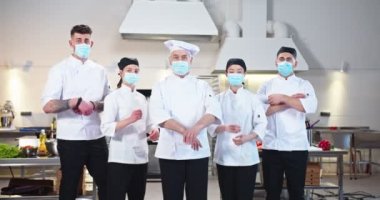 Çoklu etnik çeşitlilikteki erkek ve kadın şefler restoran mutfağında durup salgın sırasında iş gününden önce kameraya bakıyorlar. Aşçılık, iş kavramı