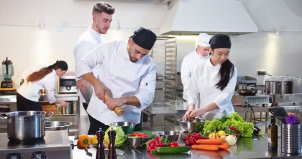 Fluxo de trabalho na cozinha da cafetaria. Equipe mista movimentada de chefs preparando comida no famoso restaurante. Caucasiano jovem cozinheiro preparar refeição no restaurante com mulher asiática colega, conceito culinário — Vídeo de Stock