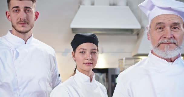 Närbild av team av professionella multietniska seniora och unga manliga och kvinnliga kockar står på restaurang kök och tittar på kameran på gott humör. Man och kvinna lagar mat. Matlagning, arbetskoncept — Stockvideo