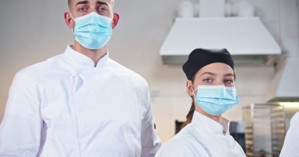 在验尸官检疫期间，一群专业的男女混血老人和年轻男女厨师站在餐厅里，目不转睛地看着戴着医疗面罩的镜头。烹调、厨师概念 — 图库视频影像