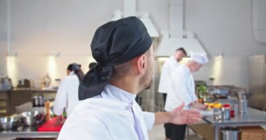 Yakışıklı, mutlu, genç bir aşçının restoranda dikilip iş akışını ve aşçıları gösteren video sohbetlerini yakından çek. Mutlu adamın iş yerinde görüntülü konuşma yapması, aşçılık konsepti.
