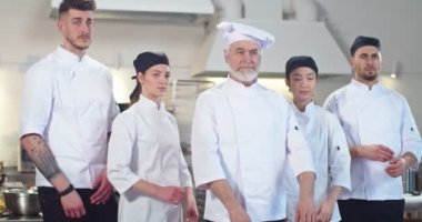 Melez ırkın portresi farklı genç ve kıdemli profesyonel şefler mutfakta birlikte poz veriyorlar. İşteki restoranda aşçı takımı. Aşçılık endüstrisi, aşçılık, meslek konsepti