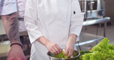 Mutlu, güzel Asyalı kadın mutfak asistanının iş yerinde restoranda durup salata yıkaması ve kameraya gülümsemesi. Olumlu duygular. Kadın aşçı yemek hazırlıyor.