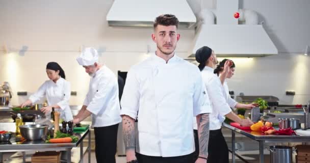 Retrato de joven caucásico guapo chef masculino serio en el restaurante. Hombre cocinero profesional en la cocina en el lugar de trabajo. Proceso de flujo de trabajo. El equipo de cocineros trabaja preparando la comida. Concepto de industria culinaria — Vídeos de Stock