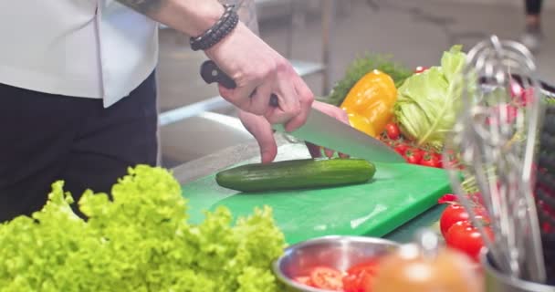 Close-up van de mannelijke getatoeëerde handen snijden komkommer werken in restaurant keuken. Chef-kok werk snijden van verse groenten, het bereiden van salade, hakken ingrediënten. Koken, culinair, beroep van kok — Stockvideo