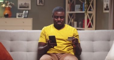Yakışıklı adam alışveriş yapıyor, akşamları evdeki internet mağazasından mobilya alıyor. Genç Afro-Amerikan kredi kartı numarasını telefonla giriyordu. E-ticaret, online alışveriş konsepti.