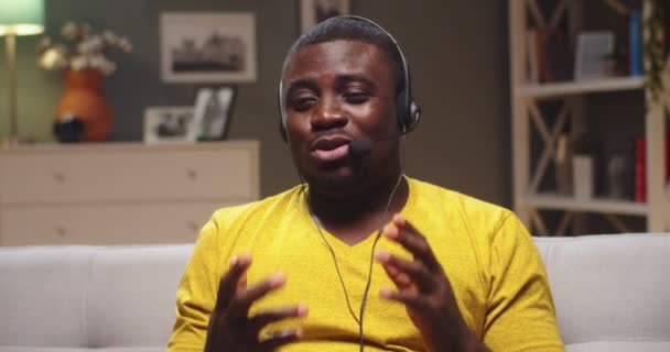 ПОВ симпатичного хлопця в навушниках з мікрофонами вдома. Афро-американський блогер транслює, розмовляє з послідовниками, глядачами ввечері. Соціальні медіа, жива, впливова концепція. — стокове відео