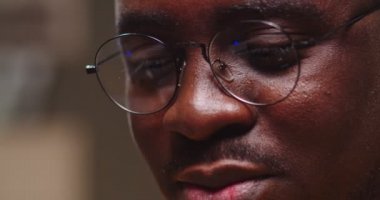 Gözlüklü adamın yüzünü kapat ve akşam evde dizüstü bilgisayar yansıması yap. Genç Afro-Amerikan bilgisayar korsanı bankaları hackliyor. Teknoloji, suç kavramı.