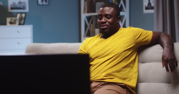 Attraktiv man som chillar på soffan och tittar på TV, senaste nytt på kvällen. Vuxen afro amerikansk kille som är upphetsad av show och glädje hemma. Underhållning, teknik koncept. — Stockvideo