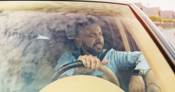 Close up de belo jovem montando carro alegremente sorrindo. Céu é refletido nas janelas do carro. Motorista feliz com barba e camisa azul desfrutar do trabalho. Estilo de vida, estrada, carro, conceito de motorista. — Vídeo de Stock