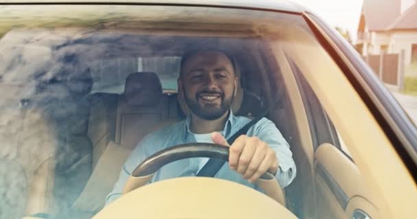 Close up of handsome young man driver riding car and listening music, moving hands in rhytm and waving to people outside. Sky reflected in windows of car. Lifestyle, road, car, driver concept. — Stock Video