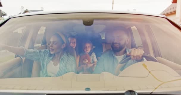 Front view of parents and their excited kids dougters with toys smiling driving car in city. Young family having fun together in car in summer. Concept of lifestyle, happy family, travel together. — Stock Video