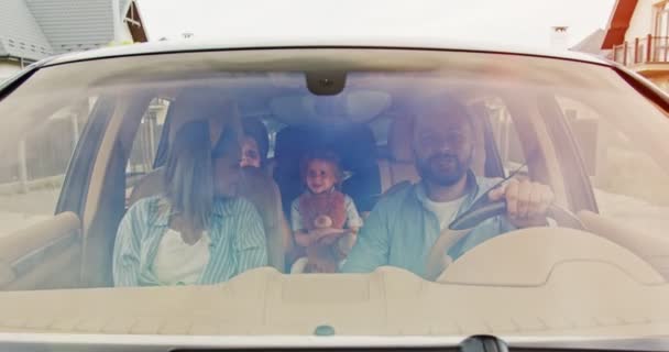 Front view of parents and their excited kids doughters with toys smiling dancing driving car in city. Young family having fun in car in summer. Concept of lifestyle, happy family, travel together. — Stock Video