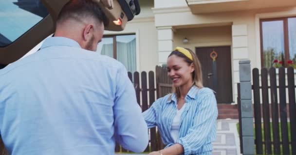 Schattig stel stapt uit de auto en laadt dozen uit naar het nieuwe huis. Volwassenen verhuizen naar een nieuw appartement in een mooie omgeving op een zonnige dag. Concept van levensstijl, gelukkig gezin. — Stockvideo