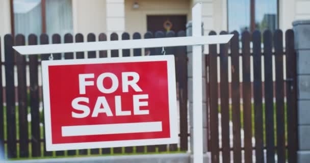 Pareja joven de pie frente a un cartel de venta mirando a su casa recién comprada. Familia mudándose a una nueva zona de apartamentos en un día soleado. Concepto de estilo de vida, familia feliz. — Vídeo de stock