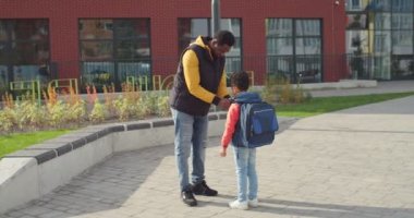 Mutlu Afro-Amerikan babası, onu okula gönderirken oğlunun kıyafetlerini düzeltiyor. Erkek ebeveyn okula ergen öğrenci getirir. Çocuk ilkokul konseptine koşuyor.