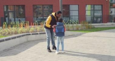 Okul bahçesindeki derslerden önce sevimli oğluna veda öpücüğü veren neşeli yakışıklı bir baba. Okula koşan sırt çantalı çocuk ve çocuğu öpen mutlu bir ebeveyn. Öğrenci konsepti