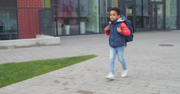 アフリカ系アメリカ人の陽気な10代の少年が学校からお父さんに屋外でクラスの後にバックパックで走って閉じます。笑顔でクラスの後に愛情のある父親に会う幸せな少年の子供。家族の概念 — ストック動画