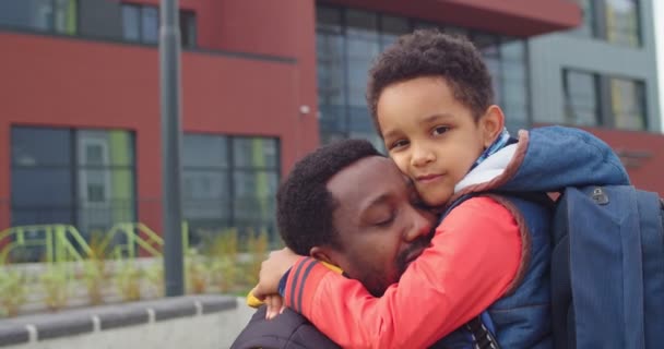 Gros plan portrait d'un enfant afro-américain aimant petit écolier mignon avec un sac à dos embrassant père et regardant la caméra. Le fils embrasse papa avant d'aller à l'école. Concept d'éducation. Objectifs familiaux — Video