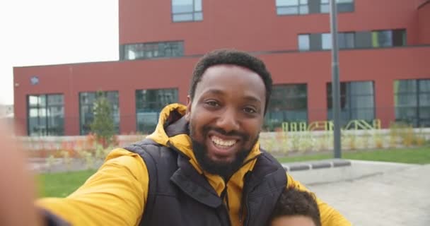 POV szczęśliwego uśmiechniętego rodzica płci męskiej i słodkiego chłopca uśmiechającego się i machającego rękami podczas nagrywania w pobliżu szkoły. zbliżenie Afroamerykanów radosny ojciec i syn mówi w Internecie wideo rozmowy. — Wideo stockowe