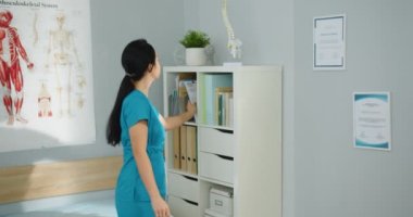 Asyalı genç kadın sağlık hemşiresinin raflardan tıbbi sonuçları alıp hastane kabinesinde imzalaması için beyaz erkek, orta yaşlı doktora vermesine yakın. Tedavi kavramı