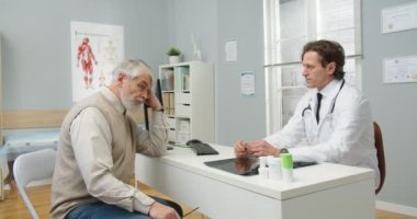 Kafkas erkek hasta, erkek doktorla doktor randevusu için hastane dolabında oturuyor. Asyalı kadın hemşire doktor belgelerini veriyor. Uzman hasta tedavisine açıklama yapıyor