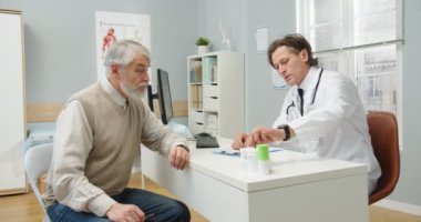 Sağlık uzmanının portresi, tıp merkezindeki masada oturmuş, beyaz erkek hastalarla sohbet ediyor, ilaç ve ilaç veriyor. Hastane kavramı