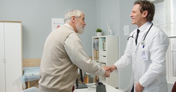 Seitenansicht. Porträt eines glücklichen kaukasischen männlichen Berufsneurologen, der einen älteren Patienten im Krankenhauskabinett trifft, der erklärt und Röntgenaufnahmen zeigt. Gesundheitskonzept. Medizinisches Zentrum — Stockvideo