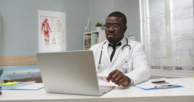 Yakışıklı, genç, Afro-Amerikan pratisyen hekimin portresi. Tıp merkezindeki kabinede oturuyor. Bilgisayarda internet üzerinde çalışıyor, daktilo yazıyor ve araştırıyor. Sağlık kavramı