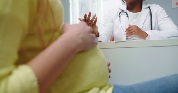 Close-up van gelukkige zwangere vrouw bezoek Afro-Amerikaanse gynaecoloog arts in het ziekenhuis of medische kliniek voor zwangerschap consultant. De dokter spreekt met een zwangere vrouw, moeder. Gynaecologisch concept — Stockvideo