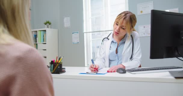 Genç bir kadının muayeneye geldiği orta boy bir fotoğraf. Hastane kliniğinde tıp alanında uzman doktor notları yazıyor. Sağlık, sağlık ve tıp konsepti — Stok video