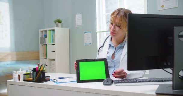 Colpo medio di donna che guarda i risultati dei test su tablet schermo verde con medico femminile in occhiali. Medico che utilizza cromakey tablet portatile per rivedere la storia sanitaria del paziente. — Video Stock