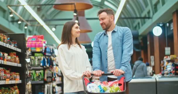 Portrait of lovely Caucasian couple with shopping cart in grocery store. Good-looking man and woman looking at camera and smiling in spermarket. Commerce, famile weekend concept. — Stok video