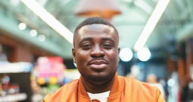 Portrait of cheerful young man in supermarket. Good-looking Afro-American male customer looking at camera and smiling. Grocery store, mall, shop in background. Shopping concept.