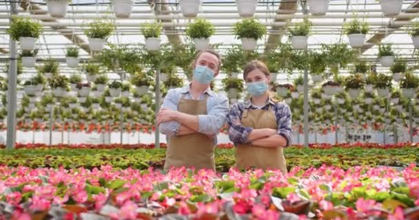 Retrato de alegre pareja de jóvenes hombres y mujeres en delantales parados en su propio invernadero, mirando a la cámara y sonriendo. Tienda de flores, empresa familiar, floristas en el trabajo en el centro de jardinería con muchas plantas — Vídeos de Stock