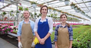 Cheerful young Caucasian positive greenhouse gardeners standing indoor at work, looking at camera and smiling. Male and female florists in aprons at workplace in garden center, floral business concept