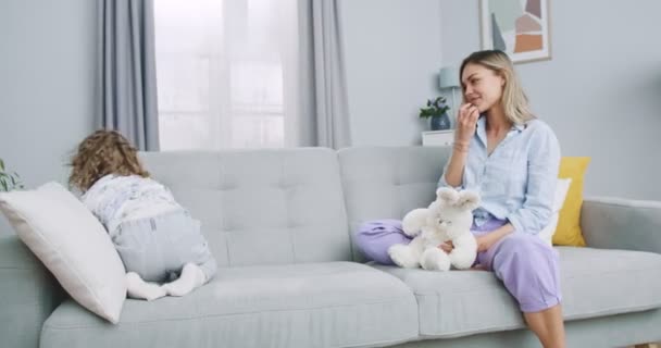 Middle plan of funny little cute girl playing favorite soft toys with nanny, waiting for parents at home. Happy small child daughter having fun with young mother, enjoying hobby pastime indoors. — Stok video