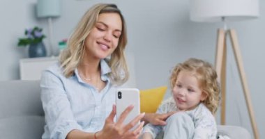 Middle plan of happy little daughter having fun with mummy enjoy using modern gadget smart phone laughing making conference call in app. Concept of family, parenthood, togetherness.