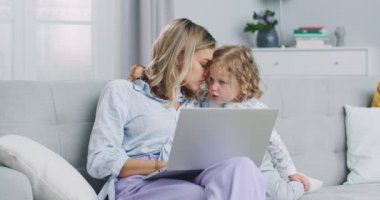 Middle plan of mother multitasking using laptop computer at home with her baby. Candide genuine and real life mom works and parenting. Self-isolation. Concept of family, parenthood, togetherness.