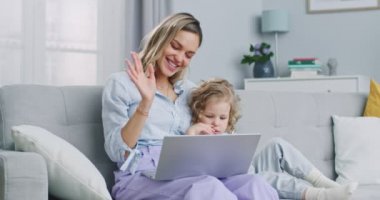 Middle plan of mother and cute child daughter making distance video call waving hands looking at camera, loving mom and kid girl smiling talking at webcam. Concept of family, parenthood, togetherness.