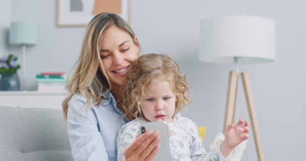 Midden plan van zoete krullend kind meisje plezier met moeder genieten van het gebruik van moderne gadget smart phone lachen kijken naar social media video. Begrip familie, ouderschap, samenzijn. — Stockvideo