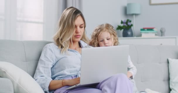 Plano medio de madre caucásica trabajando desde casa, teniendo una videollamada de trabajo, hija jugando cerca. Quédate en casa, ponte en cuarentena. Concepto de familia, paternidad, unidad. — Vídeos de Stock