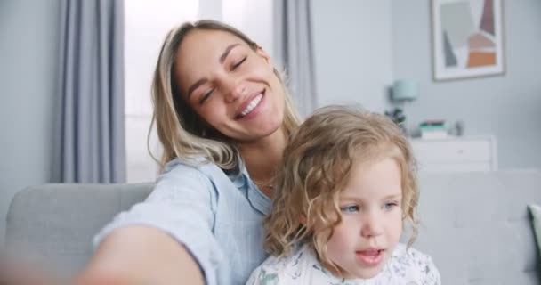 Zbliżenie szczęśliwej rodziny młoda mama i słodkie dziecko córka machając rękami patrząc na aparat wykonać połączenie wideo, matka z dzieckiem dziewczyna rozmawiając z kamery śmiech objąć komunikacji online w Internecie — Wideo stockowe