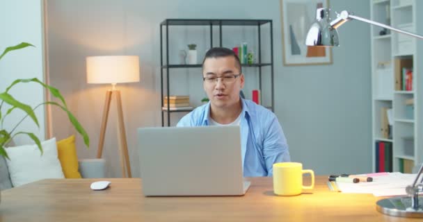 Grave joven asiático hombre de negocios hablando en video conferencia en línea en casa oficina. trabajador guapo que tiene videollamada en el ordenador portátil. — Vídeos de Stock
