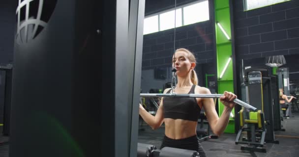 Lwów, Ukrane 04.28.2021: Silna kobieta ciężko trenująca na siłowni i ćwicząca na urządzeniu fitness. Kobieta pracująca dla tricepsów w maszynie do krzyżowania kabli. Koncepcja reklamy siłowni — Wideo stockowe