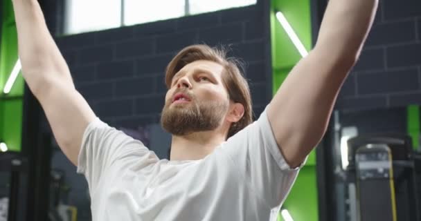 Cierre máquina de fitness trx en el gimnasio. Vista recortada de la calma activa hombres fuertes brazos de entrenamiento en el centro de actividad con una sonrisa de placer con el gimnasio con la gente en el fondo — Vídeo de stock