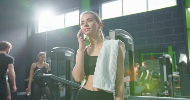 Låg vinkel syn på den starka idrottskvinna med handduk på axeln tittar på smartphone skärmen och ringa till någon efter träning. Idrott och fritid — Stockvideo
